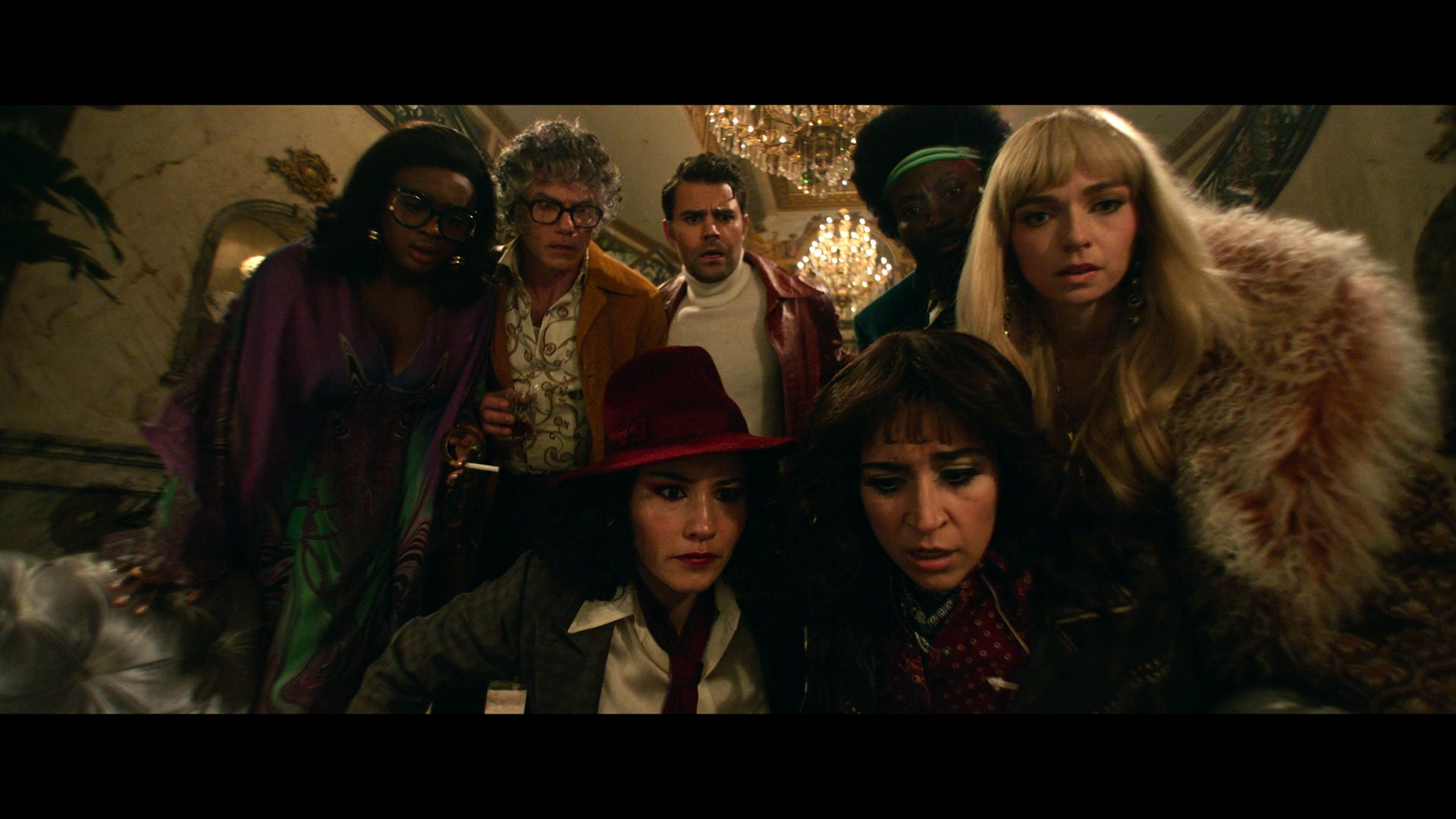 A group of diverse people dressed in vintage-style clothing are gathered closely together, appearing focused and engaged while looking at something in front of them.