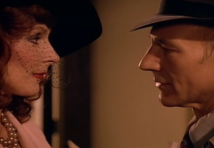 Captain Picard and Dr. Beverly Crusher are facing each other closely, dressed in vintage-style attire, with Beverly wearing a hat with a veil. There are definitely some romantic sparks.