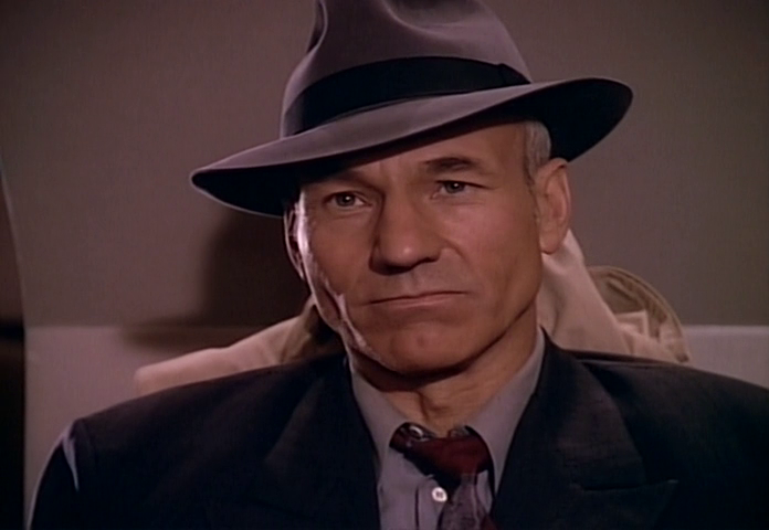 Captain Jean Luc Picard of the USS Enterprise sitting back in his chair on the bridge still wearing a suit and fedora from an adventure on the holodeck which was cut short when hostile aliens threatened the Enterprise.