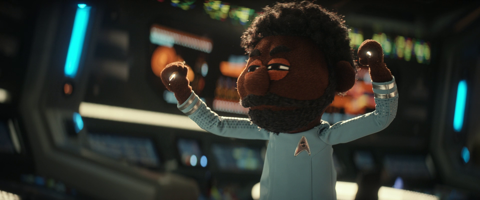 A puppet character dressed in a Star Trek uniform raises its arms on a futuristic spaceship bridge.