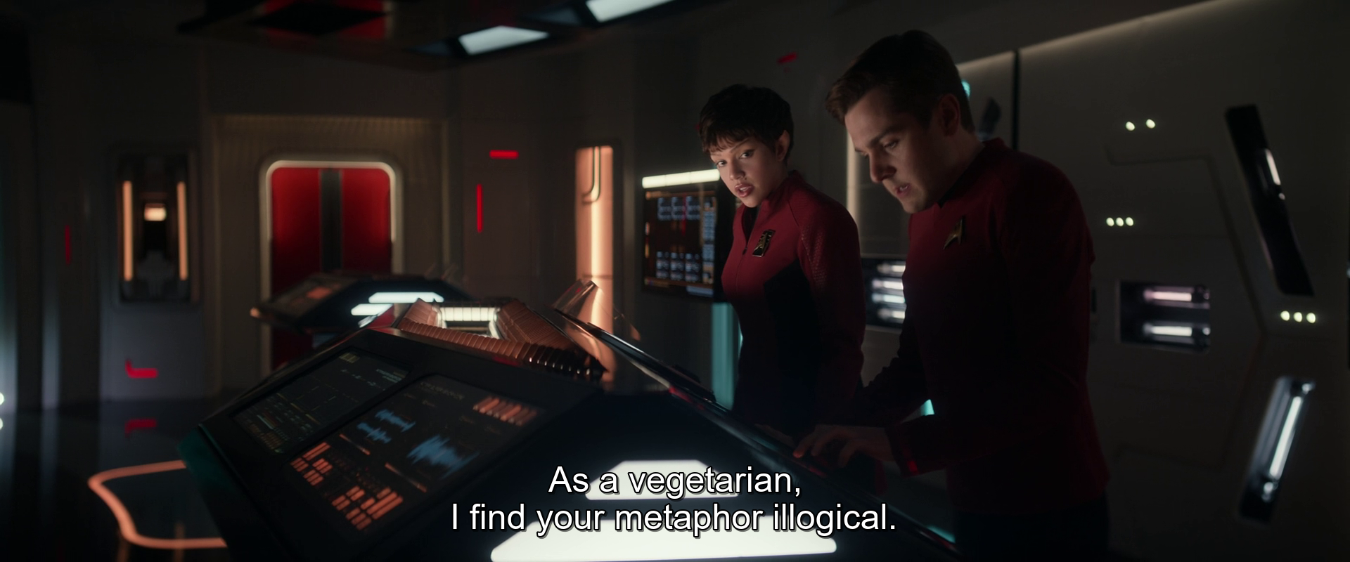 Two people in red Starfleet uniforms work at a futuristic control panel, with a subtitle reading, As a vegetarian, I find your metaphor illogical.