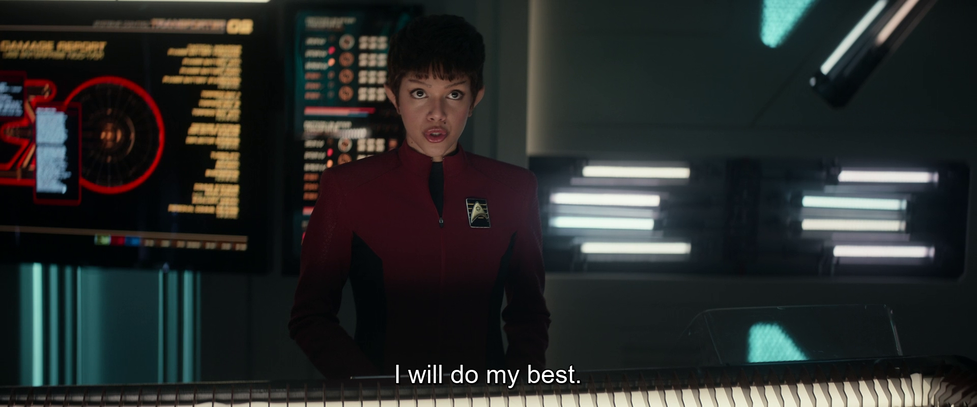 A person in a red uniform stands behind a console in a dimly lit room with futuristic screens, saying, I will do my best.